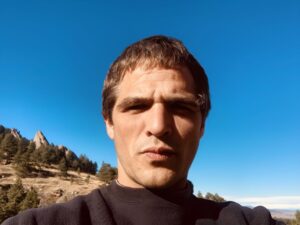 Headshot of poet Galen Cunningham outdoors with hill and blue sky